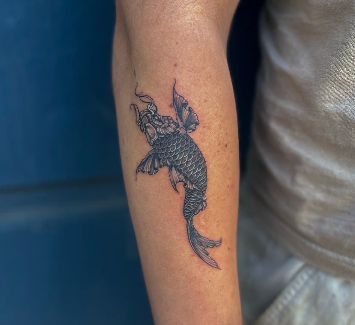 Black and grey tattoo of a koi fish on a forearm