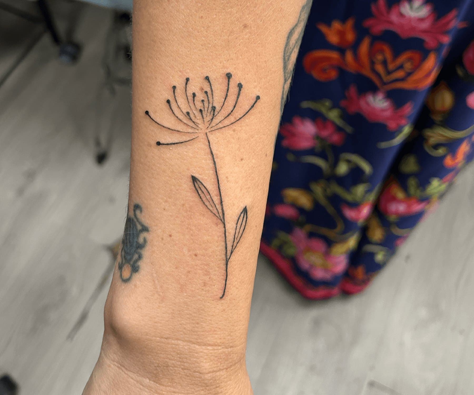 Fine line tattoo of a single wildflower on a forearm
